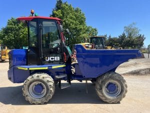Blue JCB site dumper with a red cab and large wheels parked on a construction site.