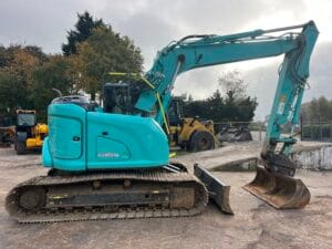 A blue excavator with a large bucket, positioned on a construction site with tracks for mobility.
